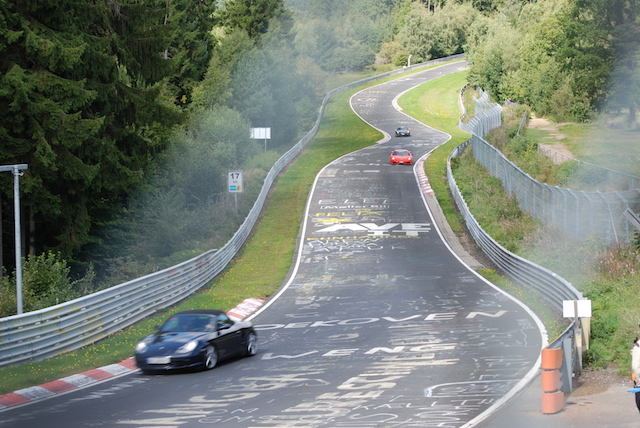 nurburgring nordschleife zelf rijden met je auto. meerdere auto's racen over het bochtige circuit met bossen aan weerszijden.