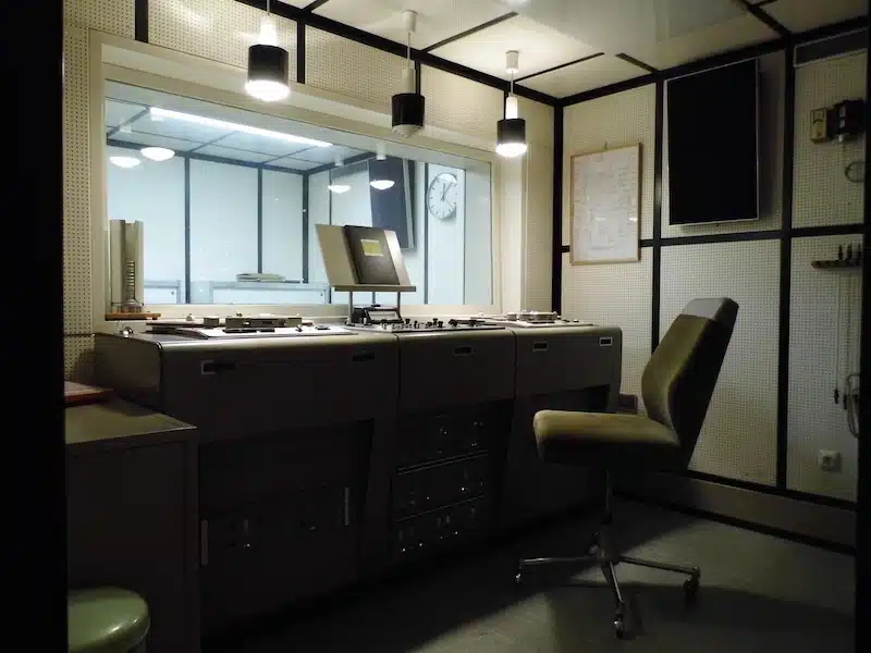 radiostudio in de bunker met alle inrichting zoals tafels, stoelen en apparatuur en een studio achter het glas