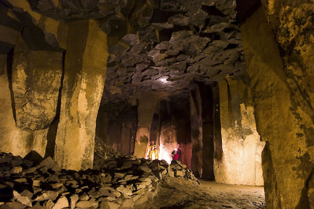 de lavakeller in Mendig. Een ondergrondse grot met rotsen en grote stenen pilaren. er is verlichting en er lopen mensen rond met zaklantaarns.