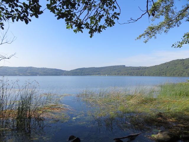 het meer met blauw water en beboste bergen op de achtergrond
