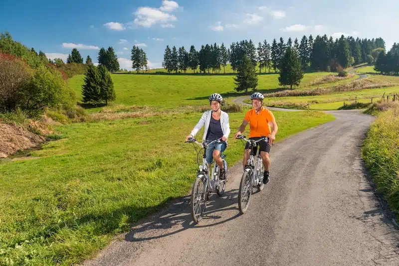 Vennbahn route. twee fietsers fietsen over een geasfalteerd pad dat slingert door de groene natuur met bossen en heuvels op de achtergrond