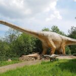 grote dinosauriër op het dinopark. levensgroot in de bossen er staan mensen onder zodat je de grote kan zien. ©Elke Wagner / Felsenland Südeifel Tourismus GmbH