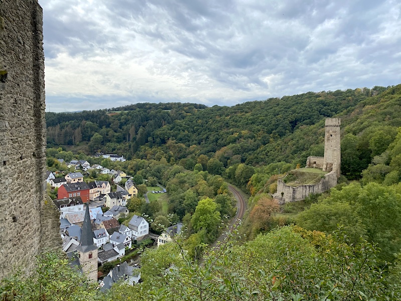 zicht op de philippsburg vanaf de löwenburg. de burchten liggen op de heuvel hoog boven het vakwerkdorpje Monreal. de spoorlijn slingert beneden door het groene bos.