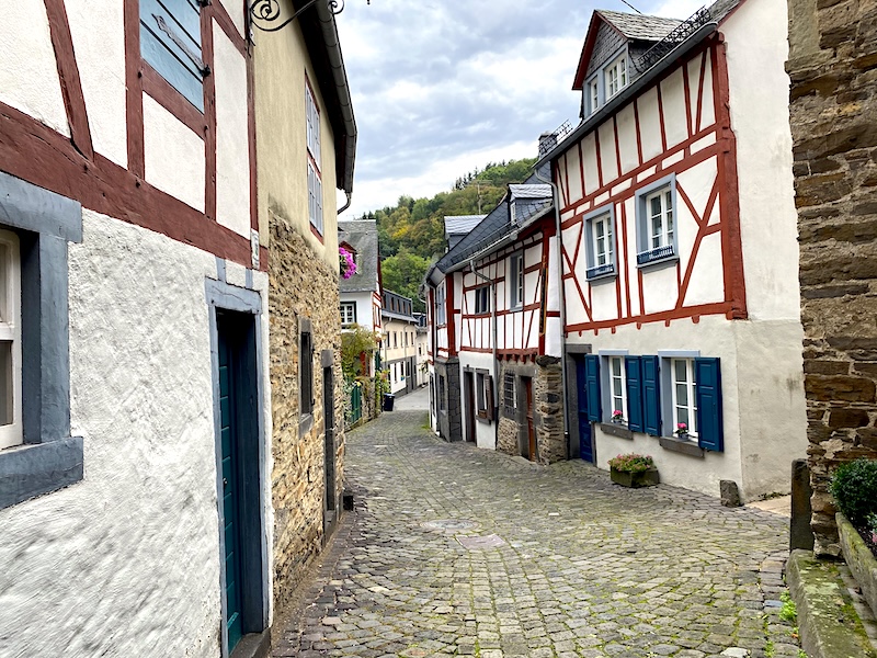 Pittoresk straatje. Smal straatje met oude klinkers die voert langs de oude vakwerkhuizen met op de achtergrond de groene heuvels van de Eifel.