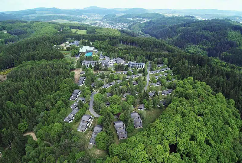 luchtfoto van sporthotel grafenwald in daun. het hotel en de vakantiehuisjes van bovenaf gezien liggend tussen het groen van de eifel