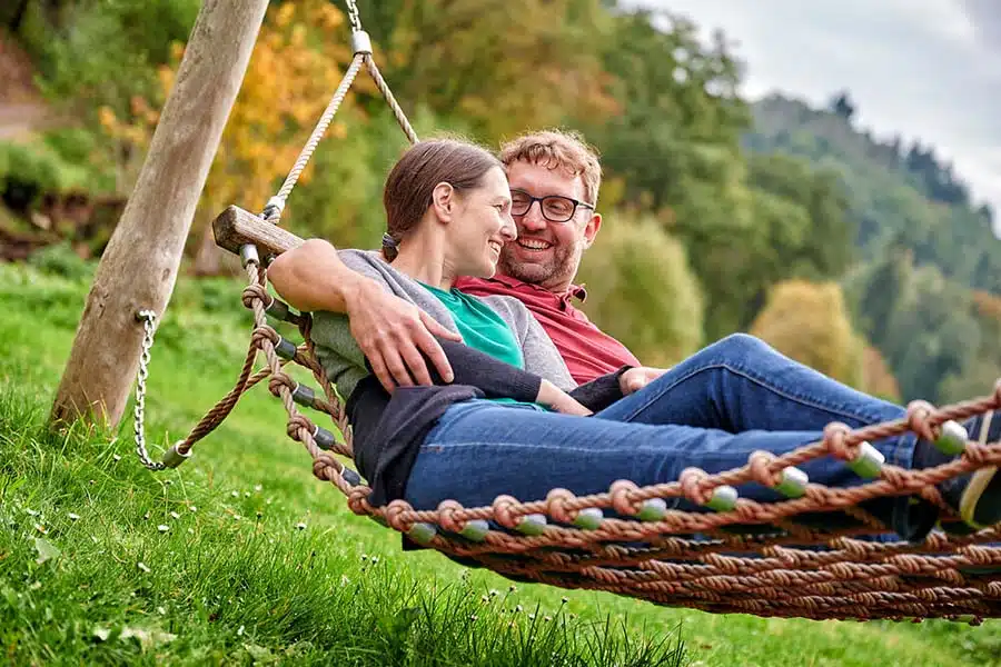 hangmat om te rusten op het HeimatSpur Achtsamkeits-Pfad Kleine Kyll. man en vrouw rusten uit in een hangmat  die in het bos hangt.