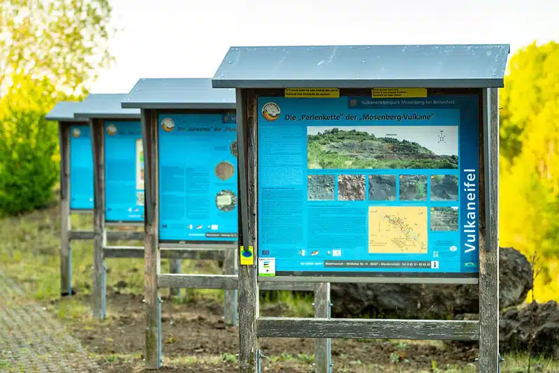 informatieborden met info over het vulkanerlebnispark mosenberg. er staan vier borden achter elkaar in een natuurlijke omgeving