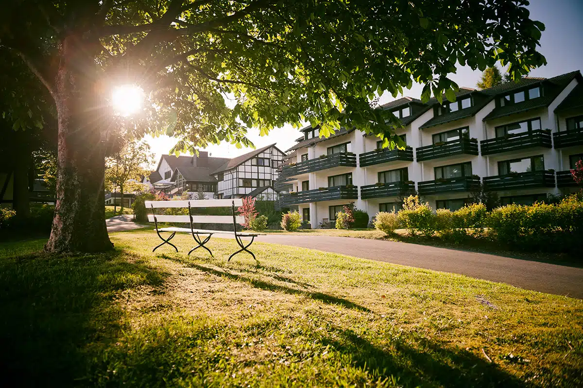 sporthotel gravenwald daun. hotel van buitenkant met boom op de voorgrond en ondergaande zon op de achtergrond