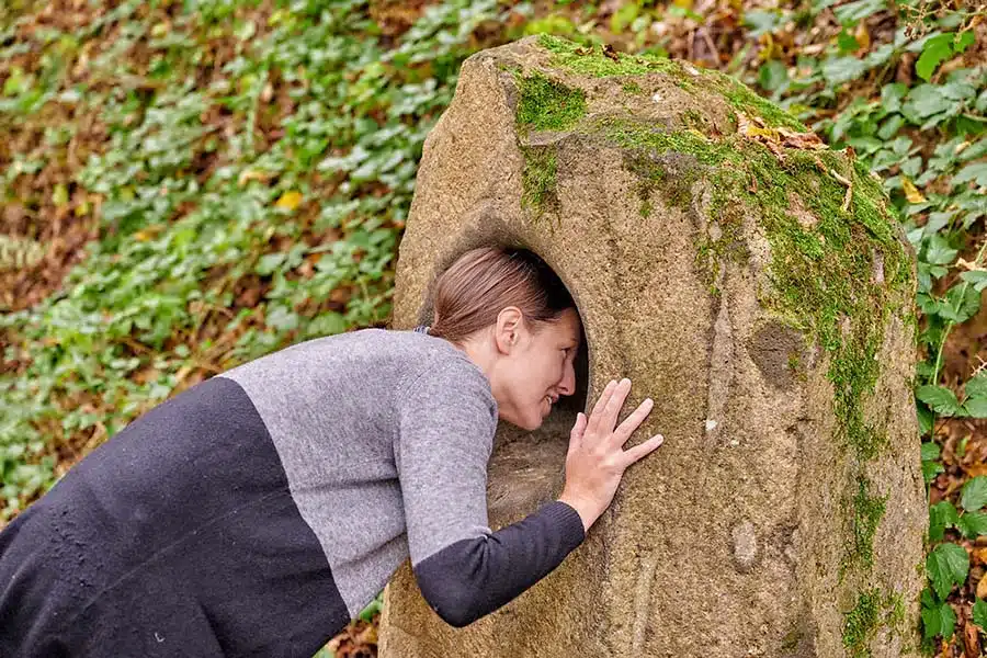 summstein bij de wandelroute bij Manderscheid. vrouw luistert naar geluiden in holle steen