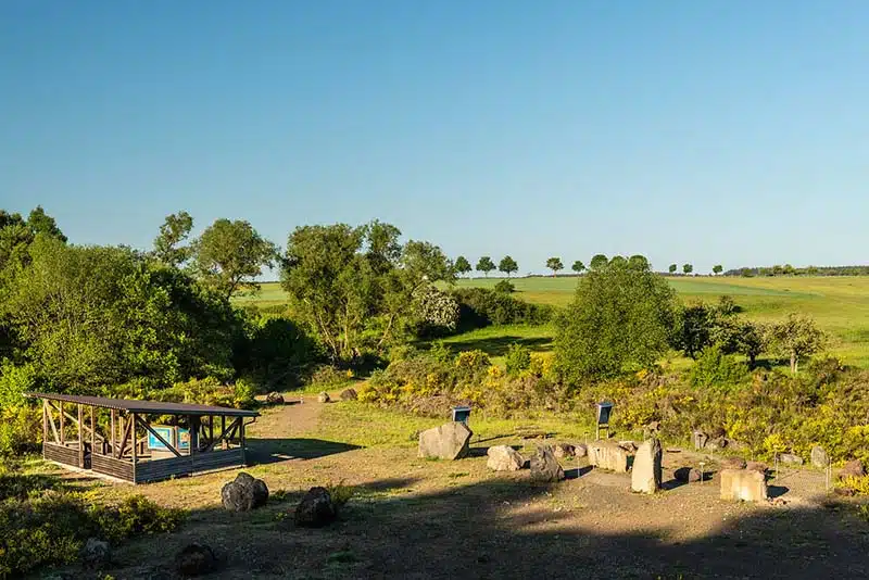 terrein met infoborden over het vulkanerlebnispark gezien vanaf de hoogte met op de achtergrond het glooiende eifel landschap op een mooie dag.