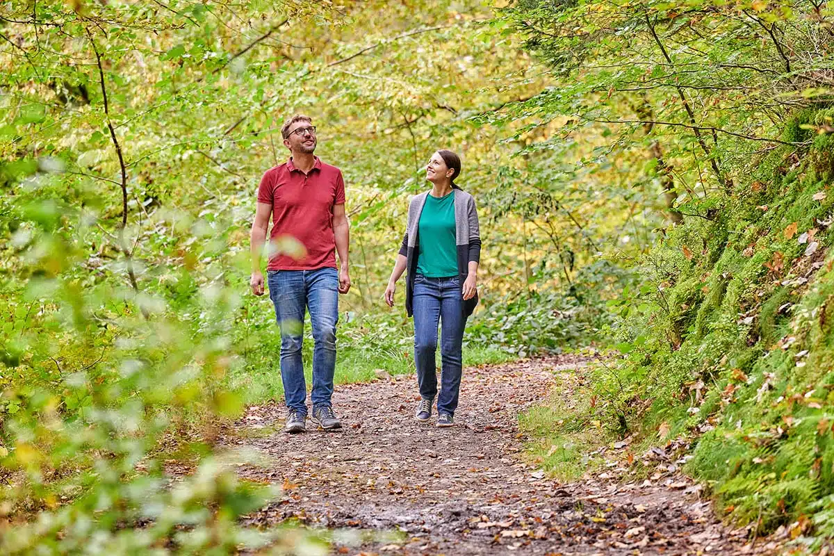 wandelen op het HeimatSpur Achtsamkeits-Pfad Kleine Kyll. man en vrouw wandelen op een pad vol met bladeren in het mooie groene bos in de eifel. foto © Florian Trykowski / Rheinland-Pfalz Tourismus GmbH