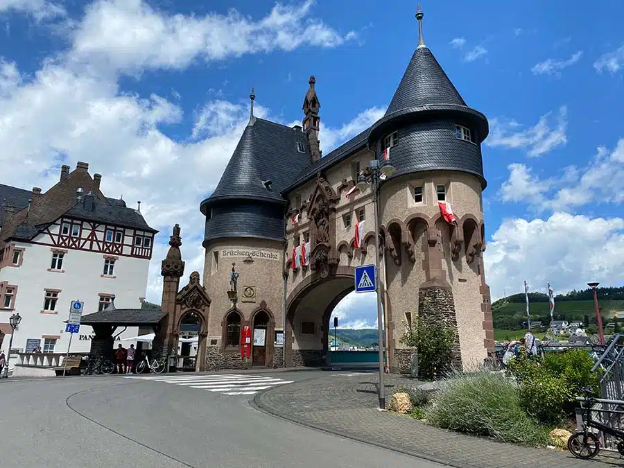 Brückentor in Traben-Trarbach. Mooie grote stadspoort met aan beide zijden torens in een prachtige oude stijl. de weg loopt onder de poort door. Er hangen vlaggen aan het gebouw en fietsers staan te kijken.