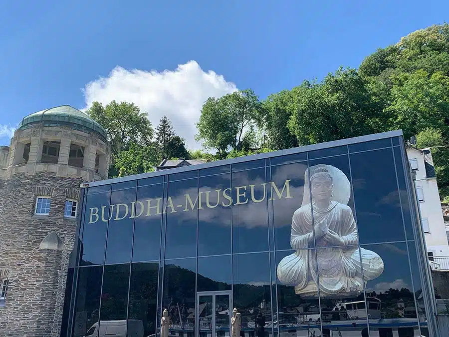 buddhamuseum in Traben. Een moderne grote glazenwand of winkelpui, aangebouwd tegen een oude toren, met een afbeelding van een Buddha beeld.