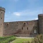 Burg Zülpich. De Landesburg is te zien vanaf de voorkant met de twee torens en de muur er tussen. op de voorgrond een grasveld en struiken en de lucht erachter is zomers blauw.