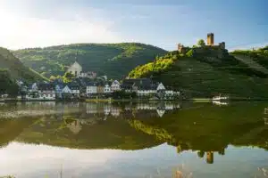 Beilstein aan de moezel. het stadje zichtbaar vanaf de oever van de moezel. het stadje weerspiegelt in het gladde water. op de achtergrond de groene heuvels met daarop het kasteel. een mooie dag met blauwe lucht. Foto © Dominik Ketz / Rheinland-Pfalz Tourismus GmbH