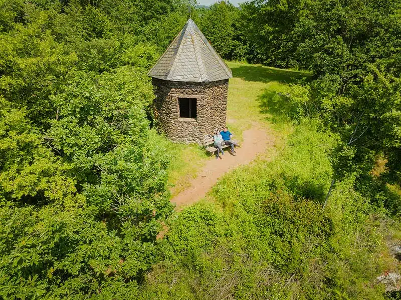 Uitzichtpunt Falkenlay bij Bad Bertrich. vanuit de lucht gezien een mooie oude stenen schuilhut met puntdak midden in het groen op een heuvel. voor het gebouwtje een bankje waarop een man en een vrouw zitten